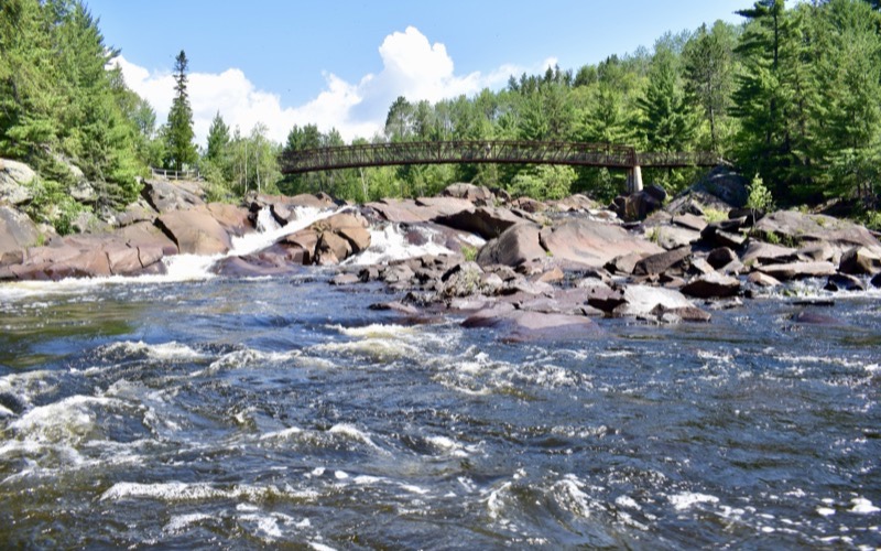 Rapids and a footbridge among pine trees in Greater Sudbury